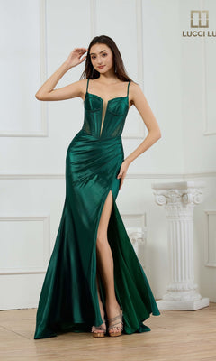 A woman poses indoors against a white paneled wall, wearing the Lucci Lu 1462 long prom dress in emerald—featuring a sleeveless satin design, corset bodice, and thigh-high slit.