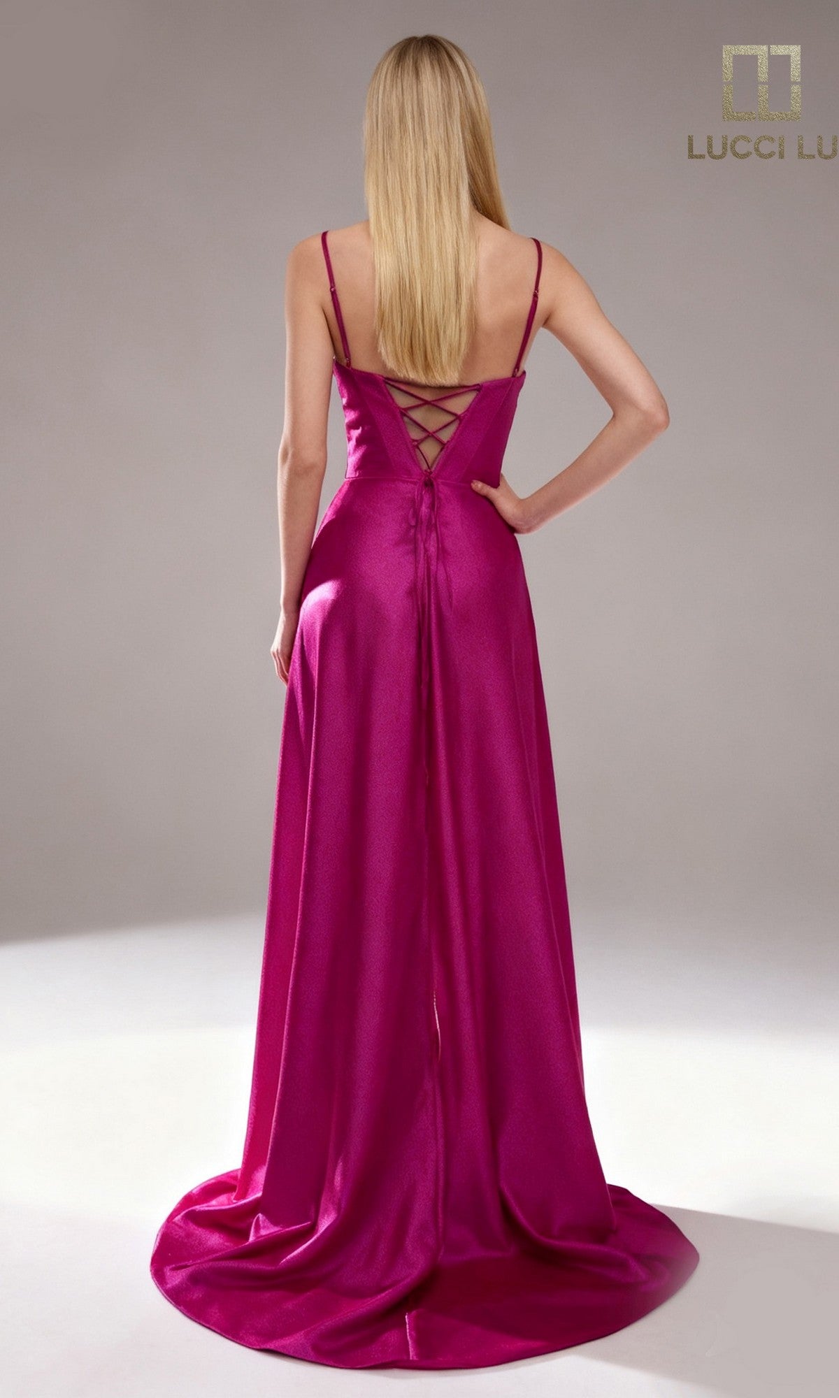 A woman stands facing away, wearing the Lucci Lu 1477 long prom dress in magenta satin with a lace-up corset bodice and thin straps.