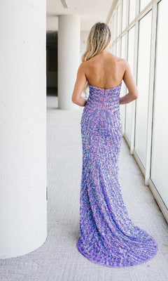 A woman with long blonde hair stands facing away in a bright hallway, wearing the Aleta 1504 Long Purple Prom Dress adorned with sparkling sequins.