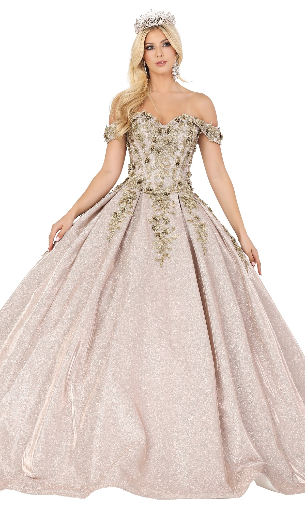 A woman stands with arms slightly extended, wearing the Quinceanera Dress 1504 by Dancing Queen—an off-the-shoulder, light pink a-line ball gown featuring lace embroidery, gold floral details, complemented by a tiara and earrings.