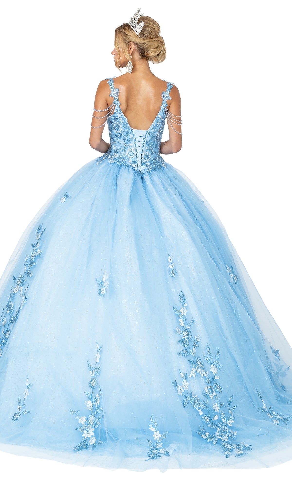 A woman in the Quinceanera Dress 1546 by Dancing Queen, featuring floral accents, beaded draped shoulder, tiara, lace-up back, and a voluminous tulle skirt, stands facing away.