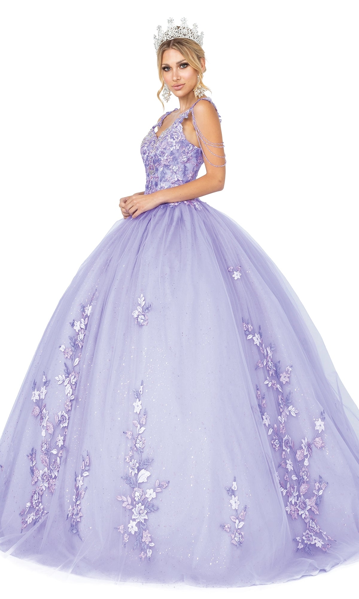 A woman in the Quinceanera Dress 1546 by Dancing Queen, featuring lavender fabric, floral appliqués, beaded draped shoulder, and a silver crown, stands against a white background.