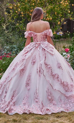A woman wearing the Glitter Quince Dress with Back Bow: Ladivine 15701, featuring floral embroidery and a large bow, stands in a garden surrounded by lemon trees and blooming flowers.