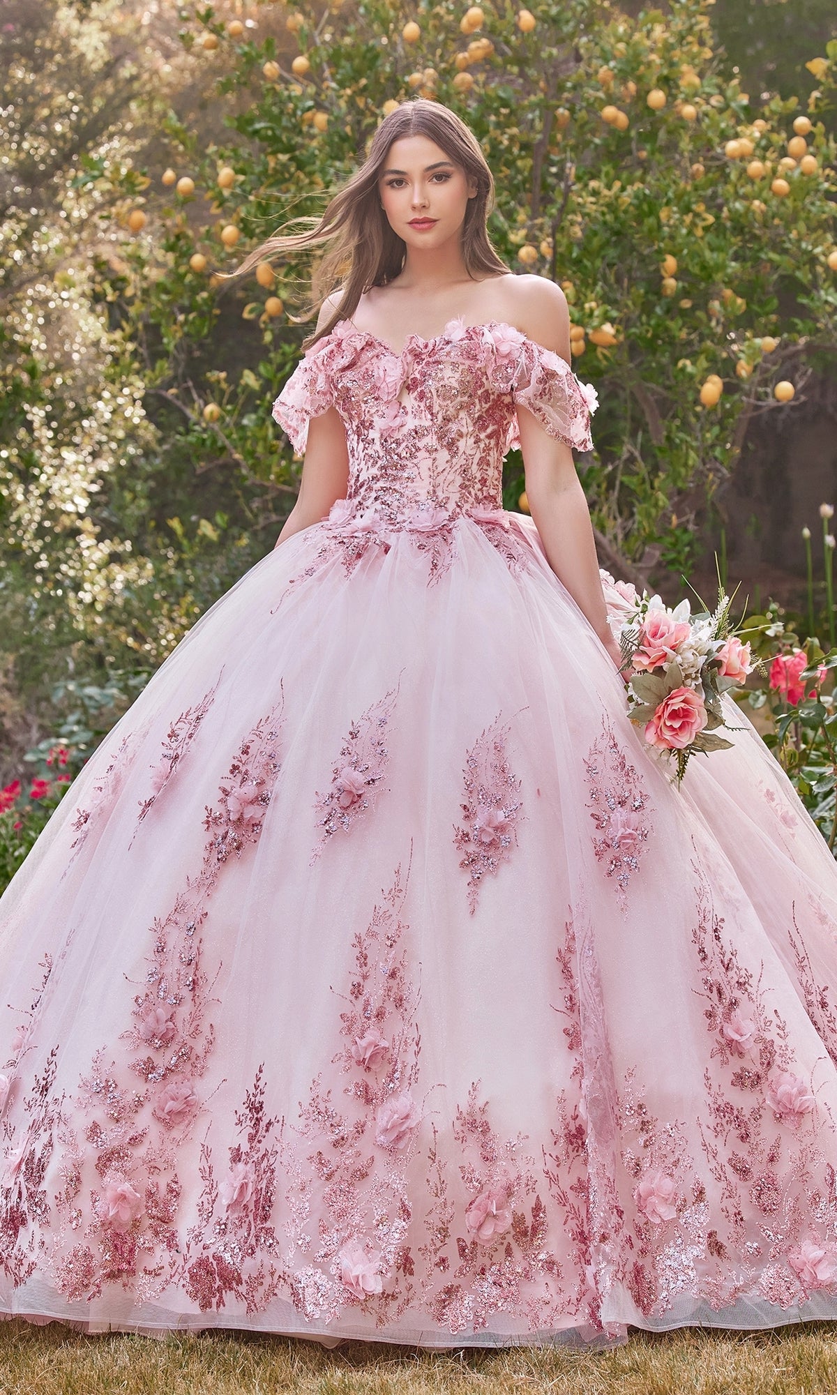 A young woman stands outdoors among greenery, holding a bouquet while wearing the Ladivine 15701 Glitter Quince Dress with Back Bow.