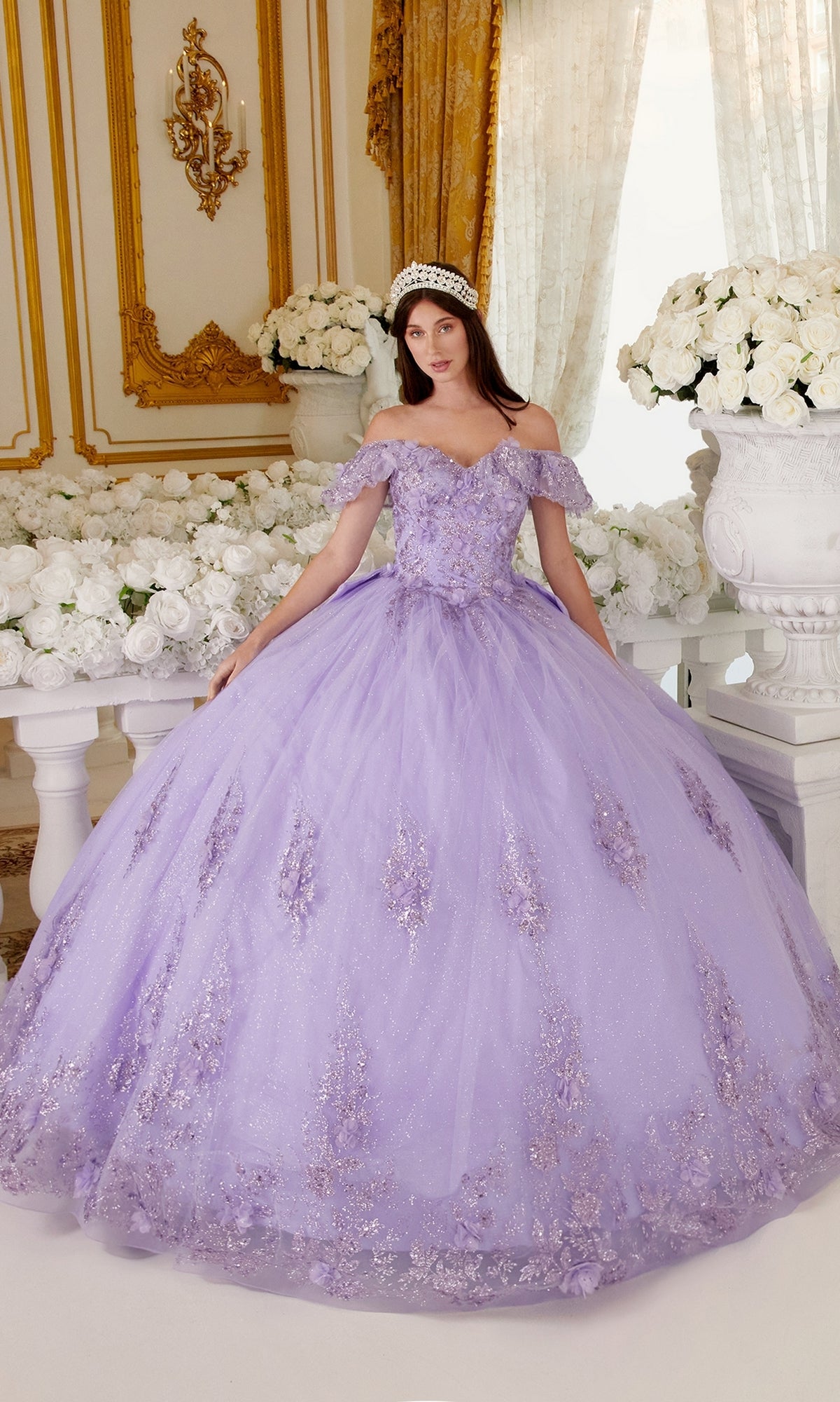 A woman poses indoors in the Ladivine 15701 Glitter Quince Dress with a back bow, wearing a tiara and surrounded by white flowers and ornate gold decor.