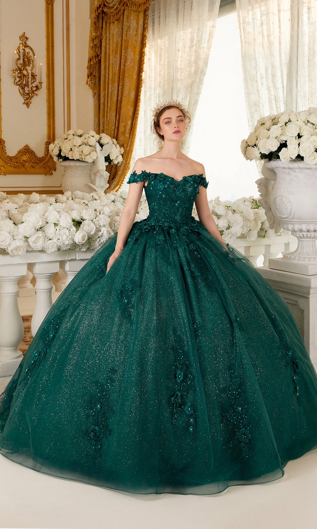 A woman in the Ladivine 15702 Quinceañera Dress with 3-D Flowers, emerald green and off-the-shoulder, stands in an ornate room decorated with white roses and gold accents.