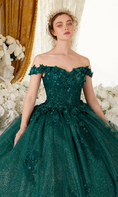 A woman in the Ladivine 15702 Quinceañera Dress—an emerald green, glittery off-the-shoulder ball gown with 3-D floral embellishments—stands before white flowers and gold curtains, finished with a regal gold crown.