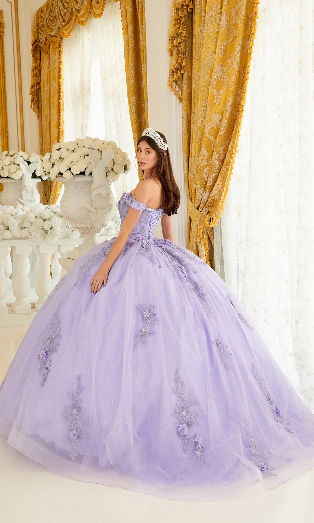 A young woman wearing the Ladivine 15702 Quinceañera Dress with 3-D Flowers and a tiara stands in an ornate room with gold curtains and white floral arrangements.