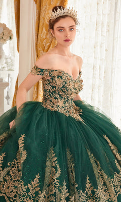 A woman wearing the Ladivine 15705 Quince Dress with gold embroidery and a tiara stands indoors before sheer curtains and gold drapes.