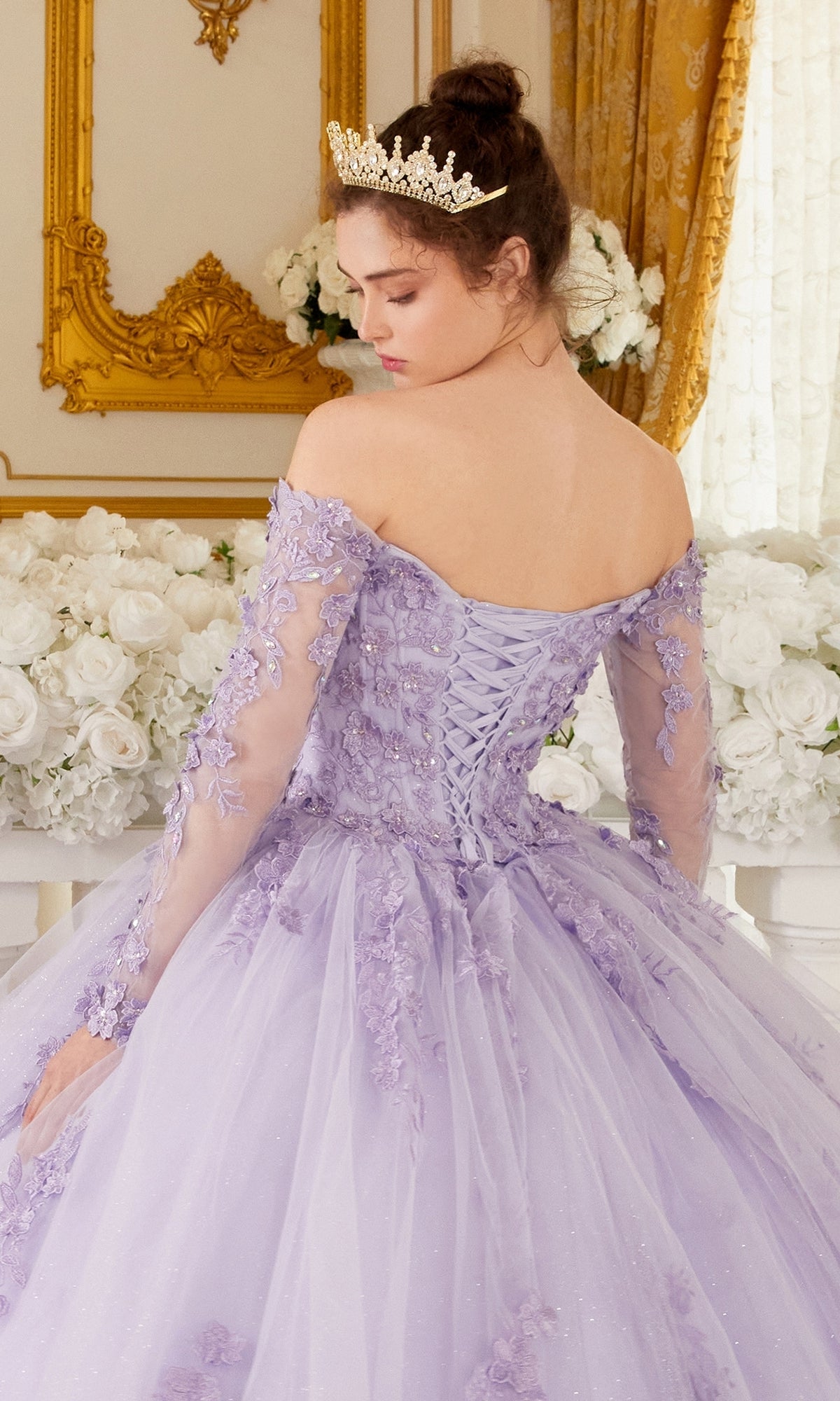 A woman wearing the Ladivine 15706 Lilac Purple Quinceañera Dress with beaded embroidery and a tiara stands in front of white flowers and gold decor, shown from behind.