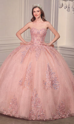 A woman in the Ladivine Strapless Quinceanera Dress 15715—sparkling pink with floral embroidery and bow detail—stands confidently, hands on hips, wearing a silver tiara in an elegant room.