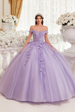 A woman stands indoors in the Off-Shoulder Purple Quinceanera Dress: Ladivine 15717, its floral details and glitter fabric sparkling among white flowers and elegant décor.