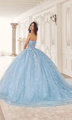 A woman in the Quinceanera Dress 15719 by Ladivine, a strapless ball gown with floral patterns, stands in an elegant white classical room, looking over her shoulder.