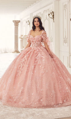 A woman stands indoors wearing the Quinceanera Dress 15719 by Ladivine—a pink, floral lace ball gown with a crown, set in a room with white walls and classical decor.