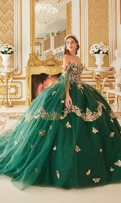 A woman in the Quinceanera Dress 15721 by Ladivine, an emerald green gown with gold embellishments, stands in a luxurious, gold-accented room featuring a fireplace and elegant flower arrangements.