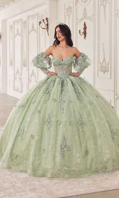 A woman wears the Quinceanera Dress 15722 by Ladivine—a light green gown with floral embellishments and removable puff sleeves—while standing in an ornate, white room.