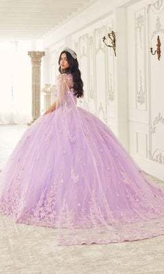 A woman in the Quinceanera Dress 15723 by Ladivine, featuring lavender floral lace applique and a corset bodice, stands in an ornate white room with a tiara, facing partially away from the camera.