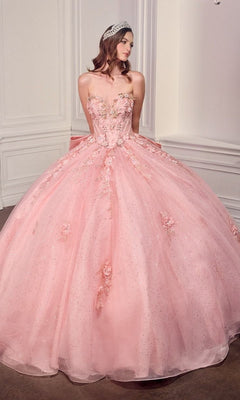 A woman in the Quinceanera Dress 15726 By Ladivine, a light pink strapless gown adorned with 3D flowers and a sparkling tiara, stands in an elegant room with white paneled walls.