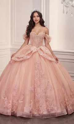A woman wearing the Quinceanera Dress 15729 By Ladivine in blush, featuring off-the-shoulder floral lace appliques, and a sparkling tiara stands in an elegant, light-colored room.