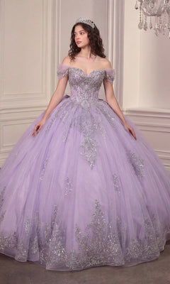 A woman wearing the Quinceanera Dress 15730 by Ladivine in lavender, featuring a crystal-embellished corset bodice and a glitter-tulle ballgown skirt with silver accents and a tiara, stands indoors against an ornate wall.