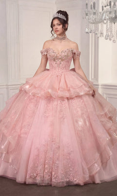 A woman stands in an elegant room wearing the Quinceanera Dress 15742 By Ladivine in pink, featuring an elaborate off-the-shoulder design with floral details and a tiara.