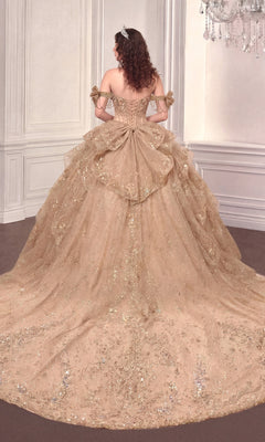 A woman in the Quinceanera Dress 15743 By Ladivine, an off-the-shoulder gold ball gown with a long, layered glittery train, stands in an ornate room with her back to the camera.