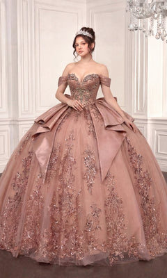 Wearing the Quinceanera Dress 15745 By Ladivine in rose, a woman stands in an elegant room with white paneled walls and a chandelier. The ornate off-the-shoulder ballgown features a beaded corset bodice and floral embellishments, while her glitter-tulle skirt shimmers as she wears a sparkling tiara.