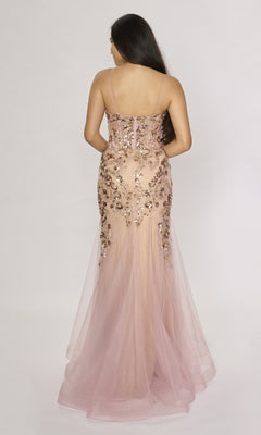 A woman stands with her back to the camera, wearing the Nina Canacci 1576 long formal dress—a sleeveless light pink mermaid gown with floral sequin embellishments and flowing tulle.