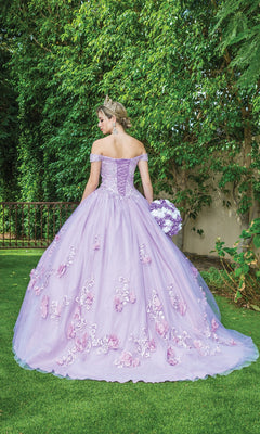 A woman wearing Quinceanera Dress 1598 By Dancing Queen, an off-the-shoulder ball gown with floral embroidery, stands on grass with her back turned. She holds a bouquet, wears a tiara, and is surrounded by lush green foliage.