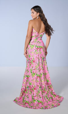 A woman wears the Tiffany 16143 long prom dress with a fitted waist, featuring a strapless floral design, as she stands and looks over her shoulder against a plain background.