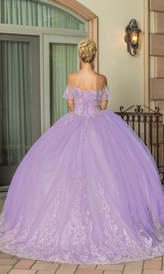 A blonde woman with her hair in an updo wears the Off-the-Shoulder Quinceanera Dress 1615, a lavender ball gown with lace embroidery, while standing outside in front of a building and window.