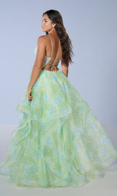 Woman wearing the Tiffany 16163 long prom dress featuring a green and blue floral print, open back, and crisscross straps, standing against a plain light background.