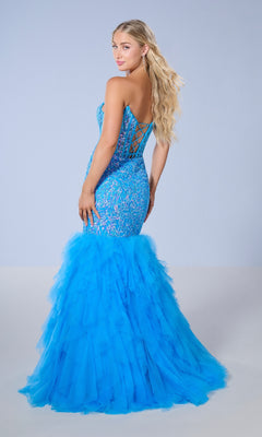 A woman models the Tiffany 16165 long prom dress, a bright blue strapless mermaid gown featuring a lace-up back and layered ruffle tulle skirt, as she stands turned slightly away against a light, plain background.