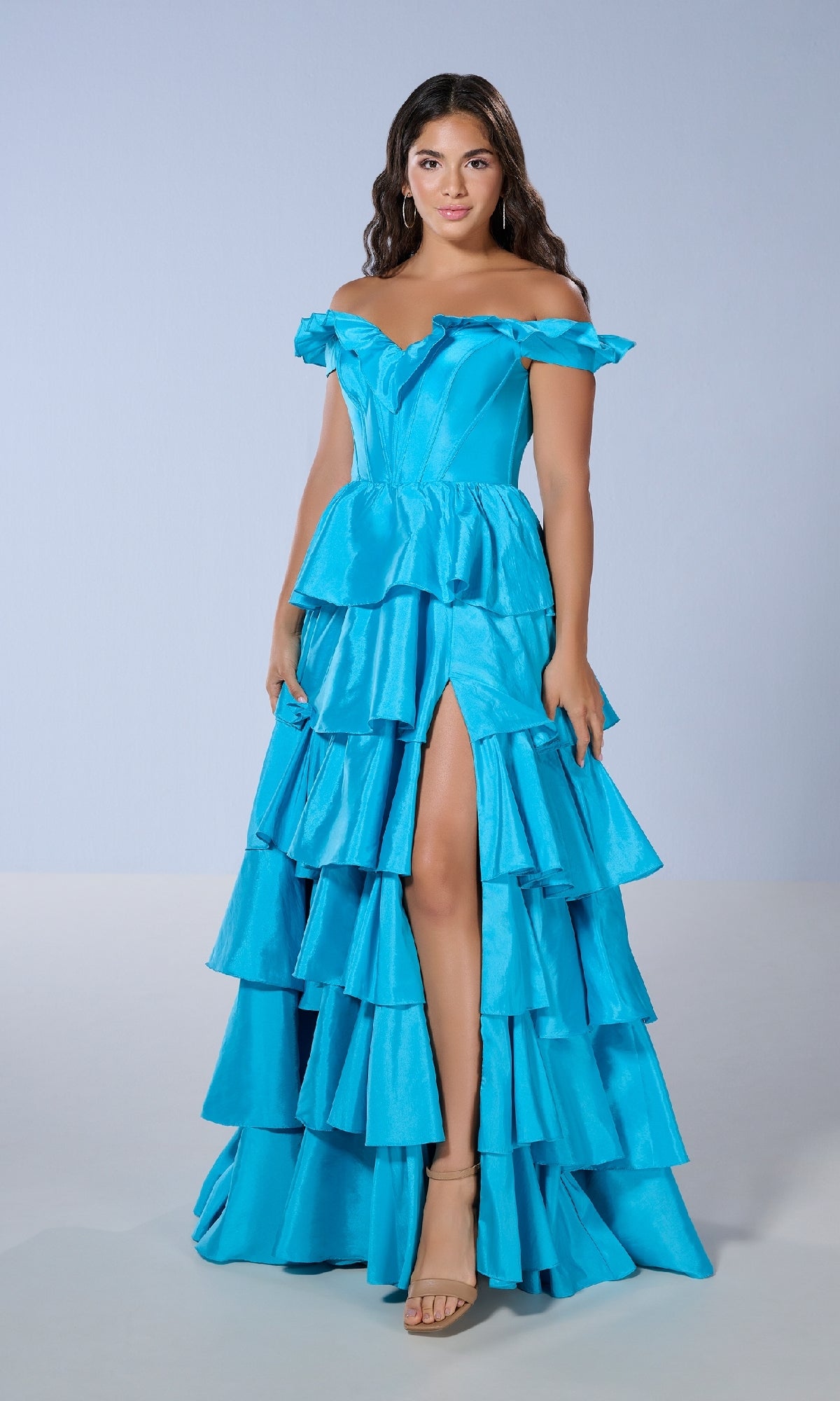 A woman models the Tiffany 16175 long prom dress, featuring a bright blue off-the-shoulder corset bodice, ruffled gown, and thigh-high slit, standing against a plain light background.