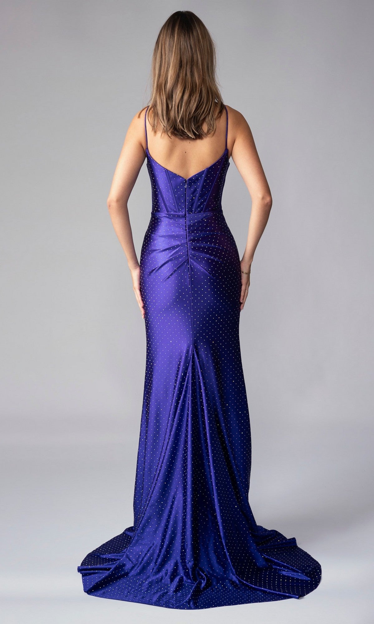 A woman faces away, wearing the Nina Canacci 1617—a long formal dress in deep blue with thin straps and sparkling embellishments—making it a stunning choice for special occasions.