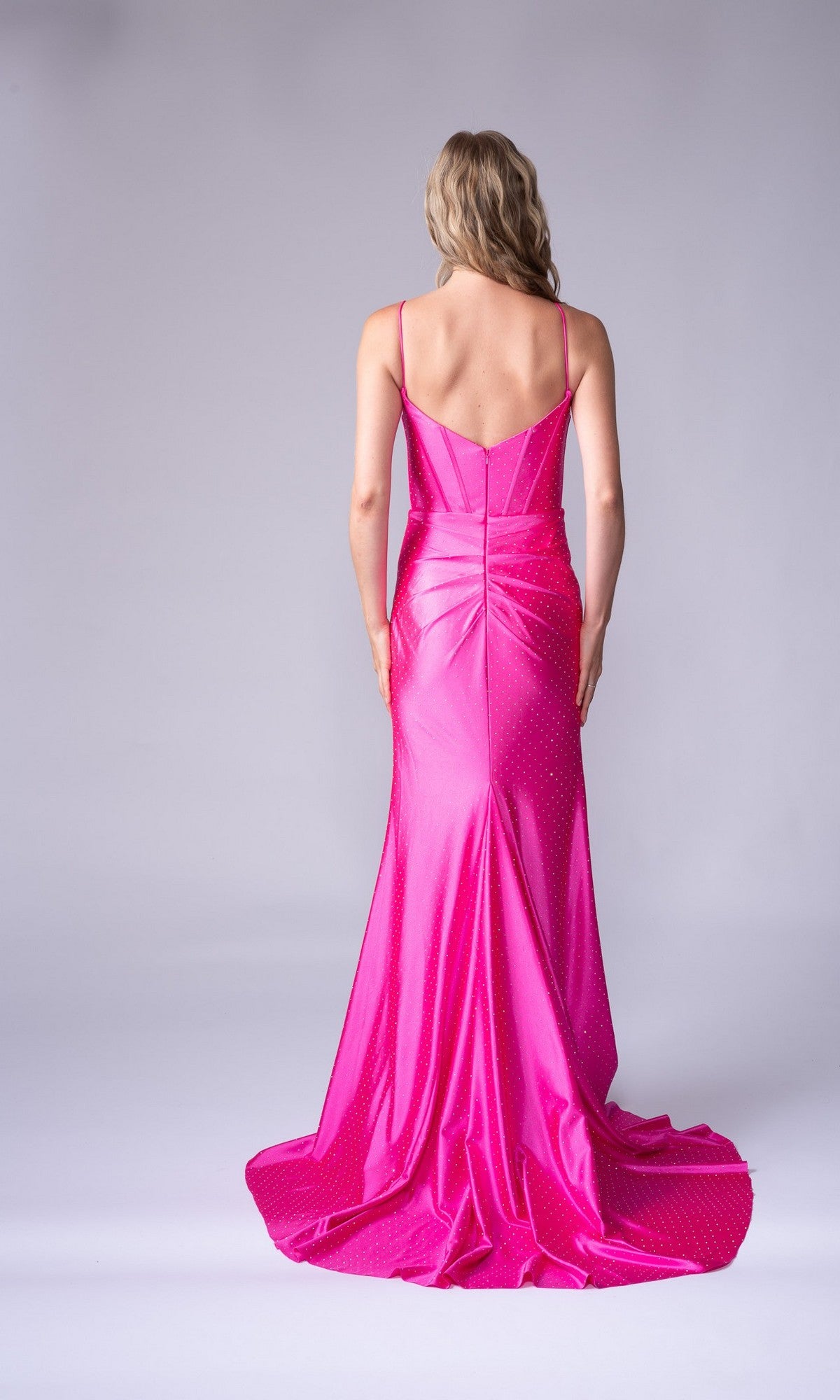 A woman with blonde hair stands facing away, wearing the Nina Canacci 1617 long formal dress featuring bright pink satin, thin straps, a corset bodice, and a fitted waist.