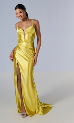 A woman in the Tiffany 16185 long prom dress, featuring shiny yellow fabric, spaghetti straps, and a high slit, pairs it with silver high-heeled sandals against a plain light background.