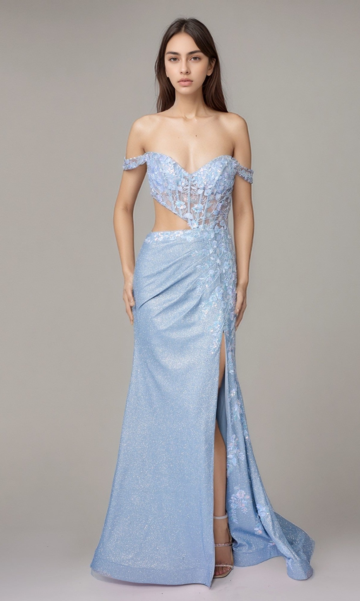 A woman stands against a plain gray background, wearing the Nina Canacci 1618 long formal dress in baby blue, featuring an off-the-shoulder corset bodice, sheer panels, floral details, and a thigh-high slit.
