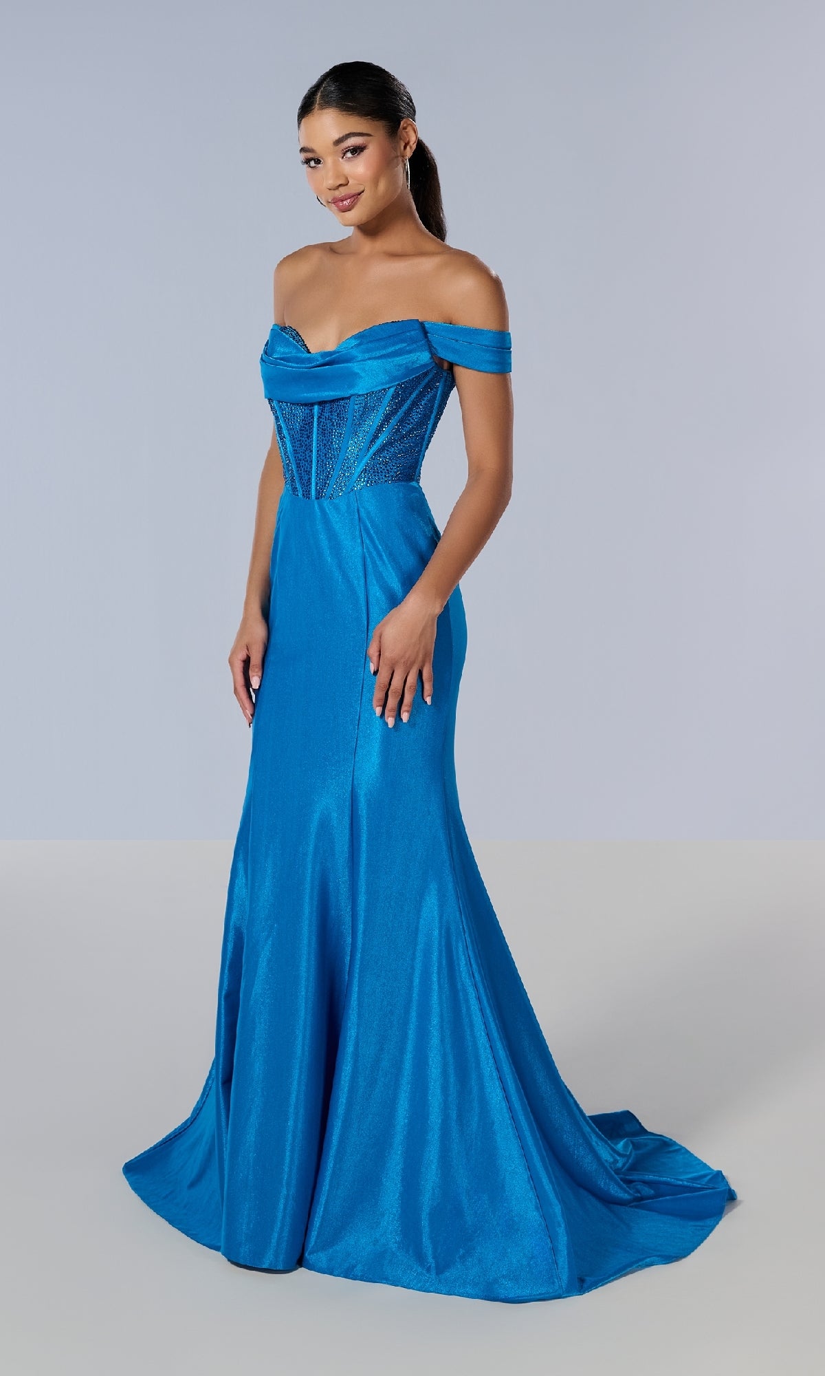 A woman poses against a plain light background in the Tiffany 16193 long prom dress, showcasing a fitted, off-the-shoulder design with a rhinestone corset bodice and flowing floor-length blue skirt.