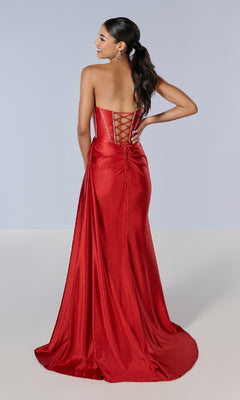 Woman wearing the Tiffany 16197 long prom dress, featuring a strapless glitter design, lace-up back, and floor-length skirt, stands with one hand on her hip, facing away from the camera.
