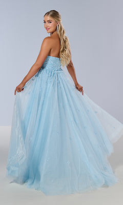 Wearing the Tiffany 16209 long prom dress, a woman stands slightly turned to the side, smiling as she holds out the full tulle skirt. The strapless design features a sweetheart neckline for an elegant look.