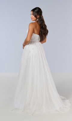 A woman with long dark hair wears the Long Prom Dress: Tiffany 16209, a strapless white gown with a sweetheart neckline, tulle skirt, and subtle embellishments, standing against a plain light background.