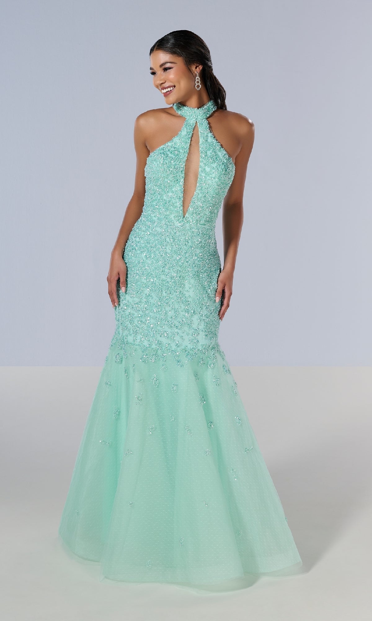 A woman stands against a plain background wearing the Tiffany 16210 long prom dress—a sleeveless, light aqua blue sequin mermaid gown with a keyhole neckline and open back.
