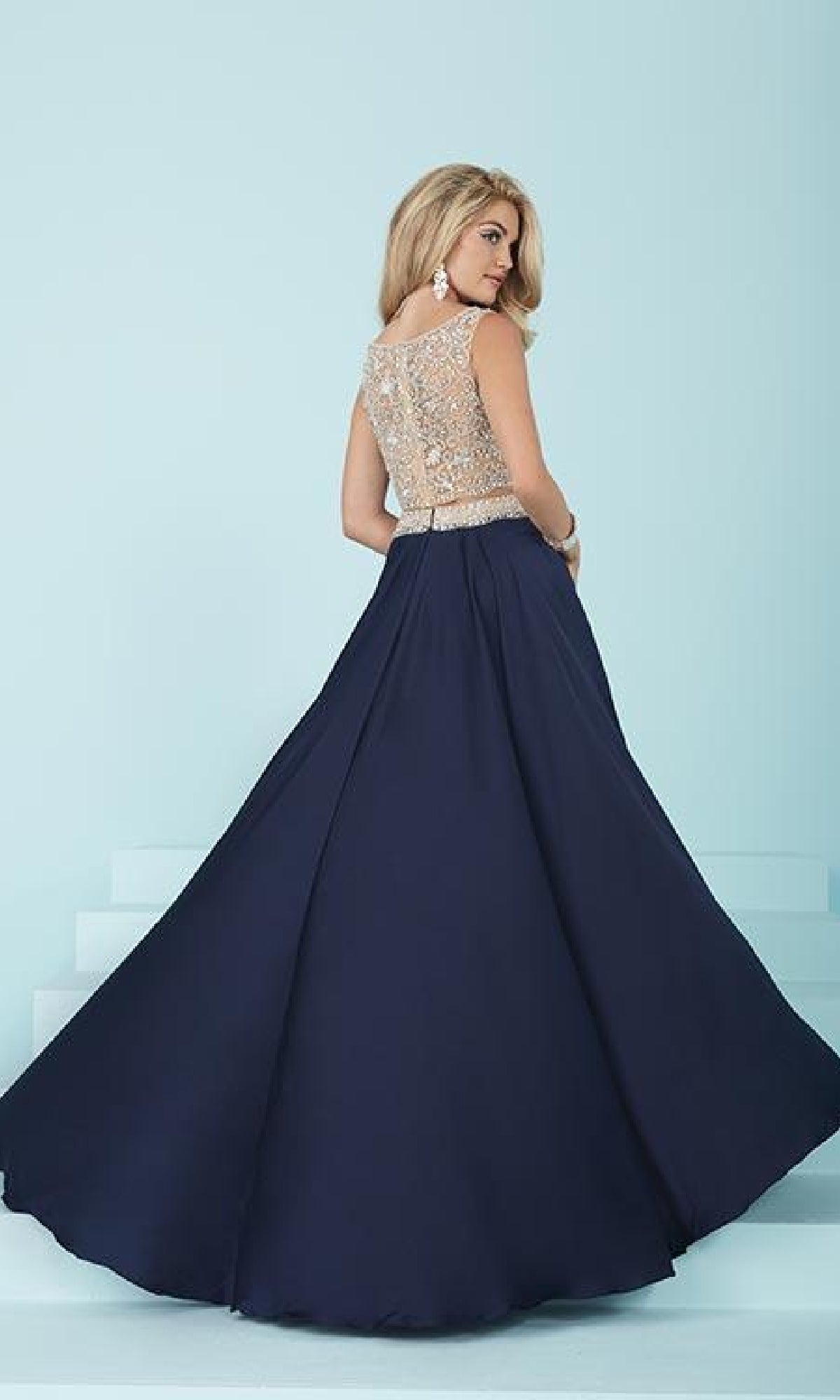 A woman stands on light blue steps with her back to the camera, wearing a navy Two-Piece Long A-Line Prom Dress featuring a beaded sleeveless top and a floor-length skirt.