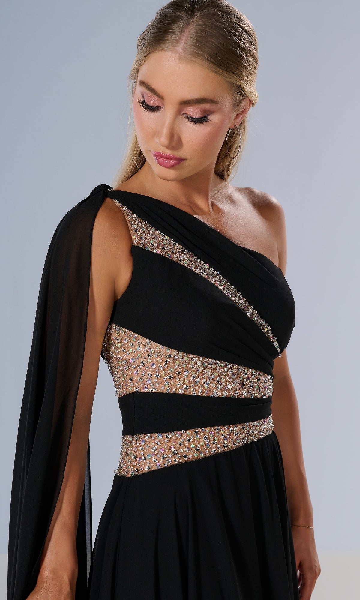 Woman wearing the Tiffany 16217 long prom dress in black, featuring a one-shoulder design, sheer sleeve, and glittering beaded embellishments, poses against a plain background.