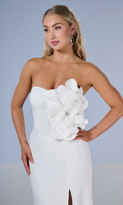 Woman models the Tiffany 16222 long prom dress, featuring a strapless design, 3D floral details, and a thigh-high slit. She poses confidently with one hand on her hip against a plain background.