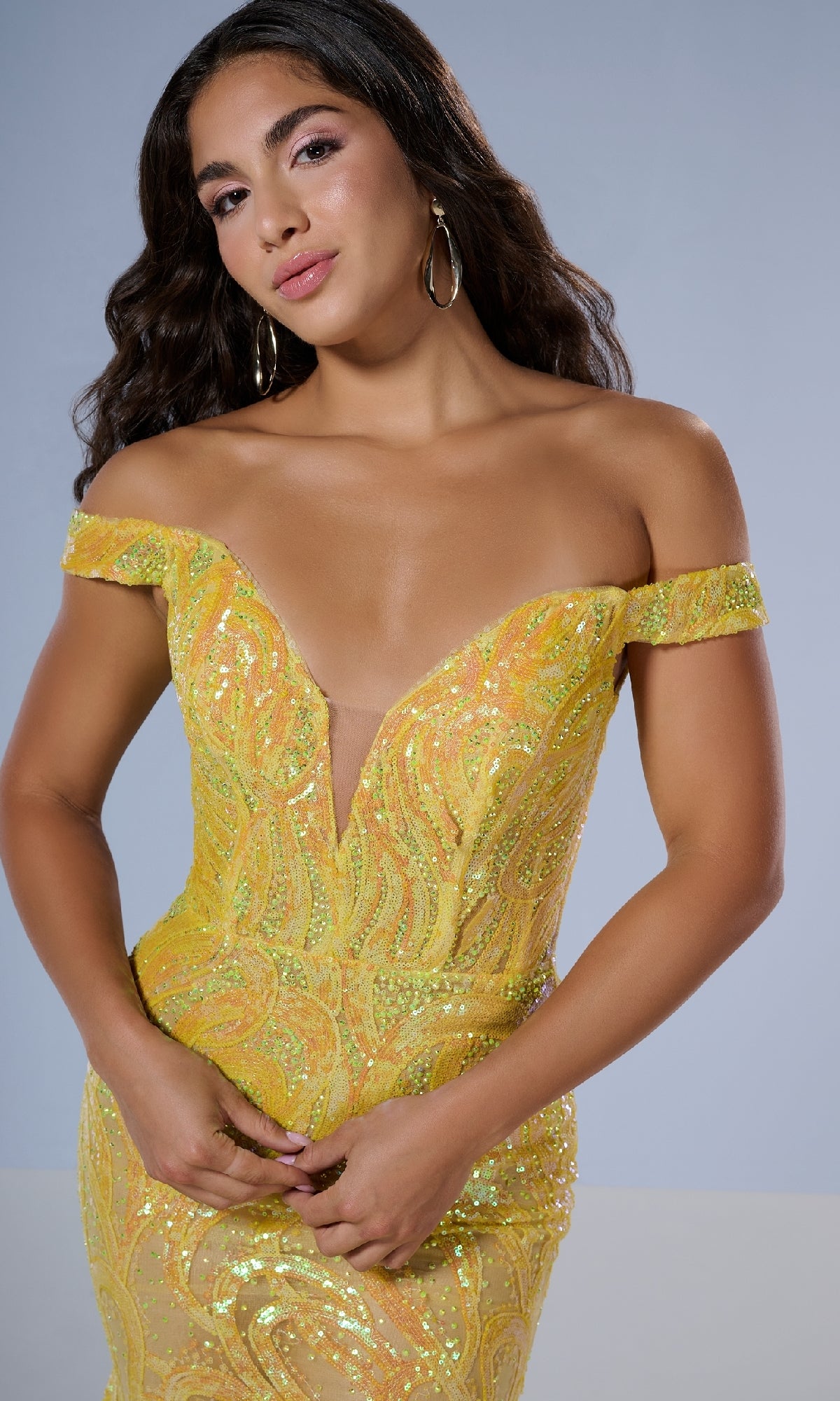 A woman in the Tiffany 16224 long prom dress—a shimmering yellow sequin gown with a deep neckline, off-the-shoulder style, and graceful mermaid silhouette—stands against a plain background.
