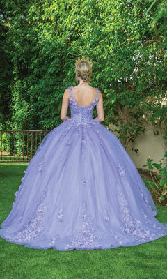 A woman in the Quinceanera Dress 1623 by Dancing Queen and a tiara stands on grass with her back to the camera, facing a lush, leafy green background.