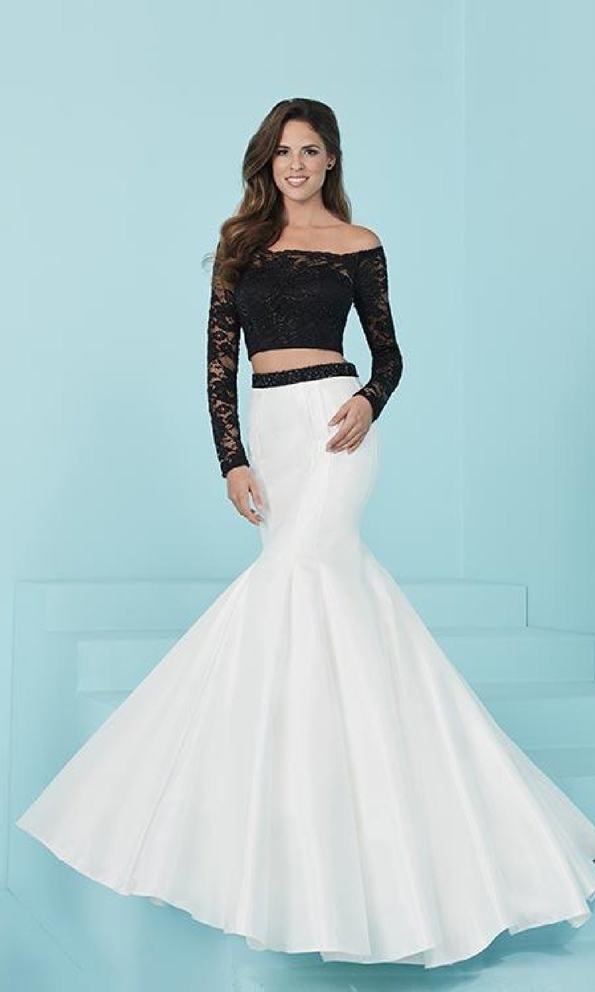 A woman poses against a light blue background in the Two-Piece Mermaid Prom Dress with Lace Sleeves, featuring a chic off-the-shoulder lace top and a flared white high-waisted skirt.
