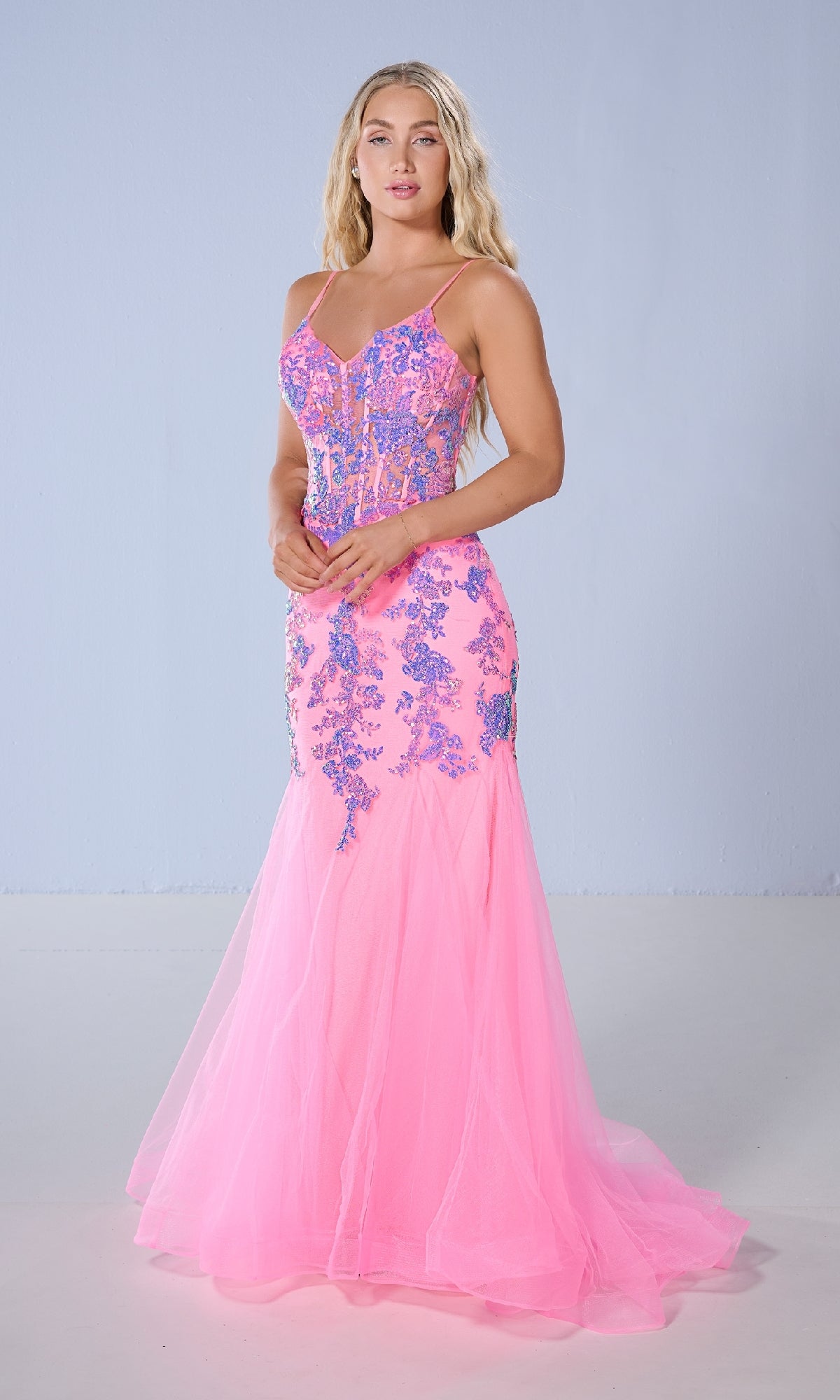 A woman poses against a light blue background in the Tiffany 16240 long prom dress—a floor-length pink mermaid gown with blue floral sequin appliqué and thin straps, capturing classic Tiffany Designs glamour.